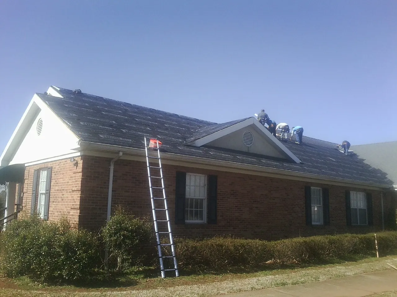Crew tearing shingles off a brick ranch roof with a ladder set — Emergency Roof Repair work by our crew in Gunpowder