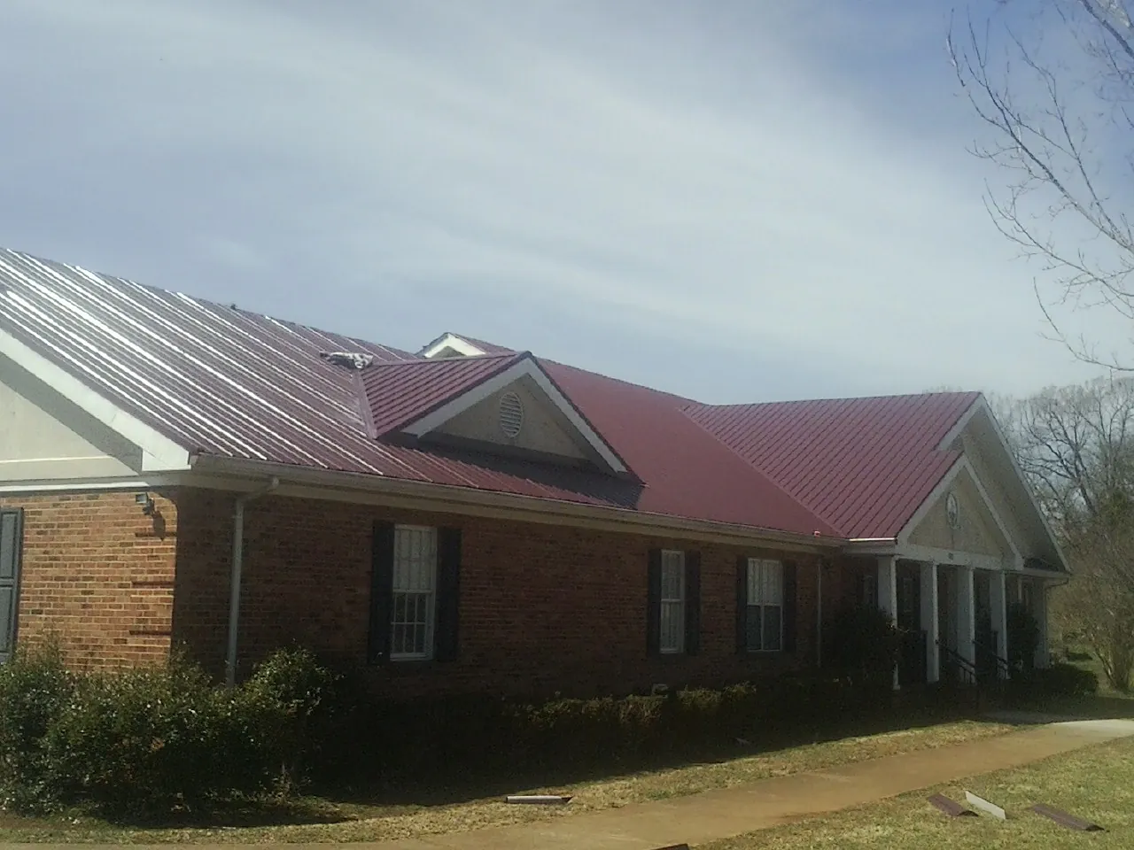 Red metal roof with gabled entries on a long brick building, from a Hail Damage Roof Repair job in Gunpowder