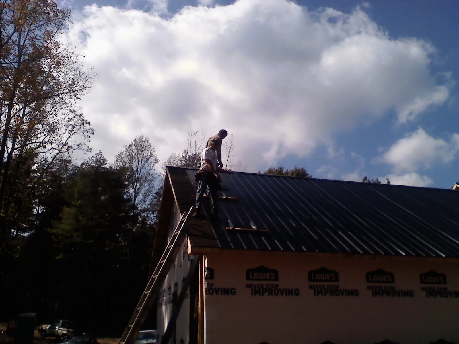 Roofer fastening dark metal panels high against a cloudy sky, from a Roof Inspection job in Gunpowder