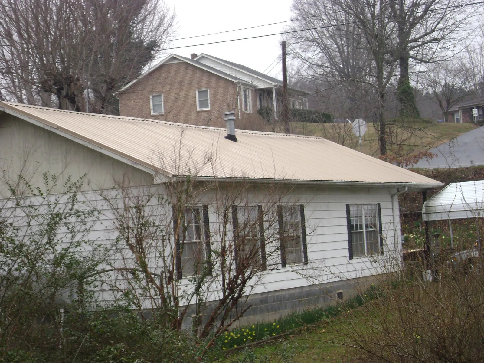Tan metal roof on a white sided house set into a hillside — Commercial Roofing by Roofing Brothers in Gunpowder